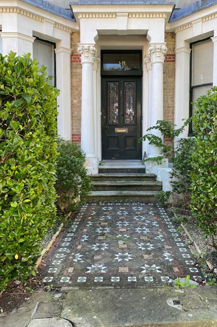 A front entrance to a period property in Knightsbridge with a black wooden door framed by classical white columns and decorative molding, accessed via a short flight of three stone steps. The pathway 